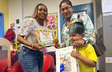 A woman reads a picture book to the babies on her lap.