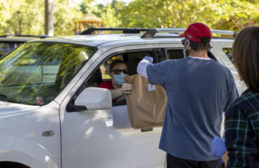 Winterville, Georgia - May 16, 2020: During the COVID-19 pandemic volunteers wearing protective masks and gloves distribute pre-paid orders at a customer drive-up at the Marigold Market in Pittard Park. A full opening for the new weekly community market is on hold until shelter-in-place restrictions are lifted.
