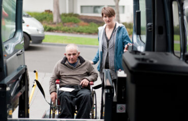 Man in wheelchair entering a modified van shot from inside the vehicle, and with a female support worker by his side.