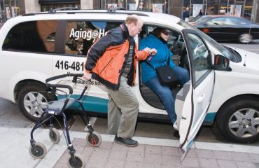 Assistant helping disabled person on wheelchair with transport using accessible van ramp